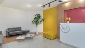 Una recepción moderna con un sofá, una mesa de centro, una planta en maceta y un mostrador de recepción con un logotipo.