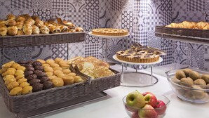 Un bufé con diversos productos de pastelería, como bollos, muffins y un pastel, presentado sobre una mesa con baldosas estampadas al fondo.
