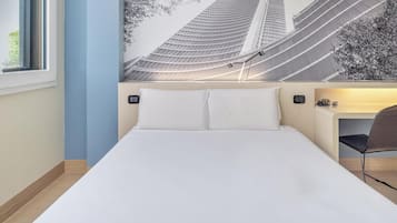 Ein Hotelzimmer mit einem Bett, einem Sessel, einem am Wand befestigten Fernseher und einem Fenster.