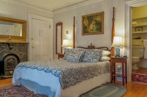 A bedroom with a bed, two bedside tables with lamps, a painting on the wall, a door, and a fireplace.