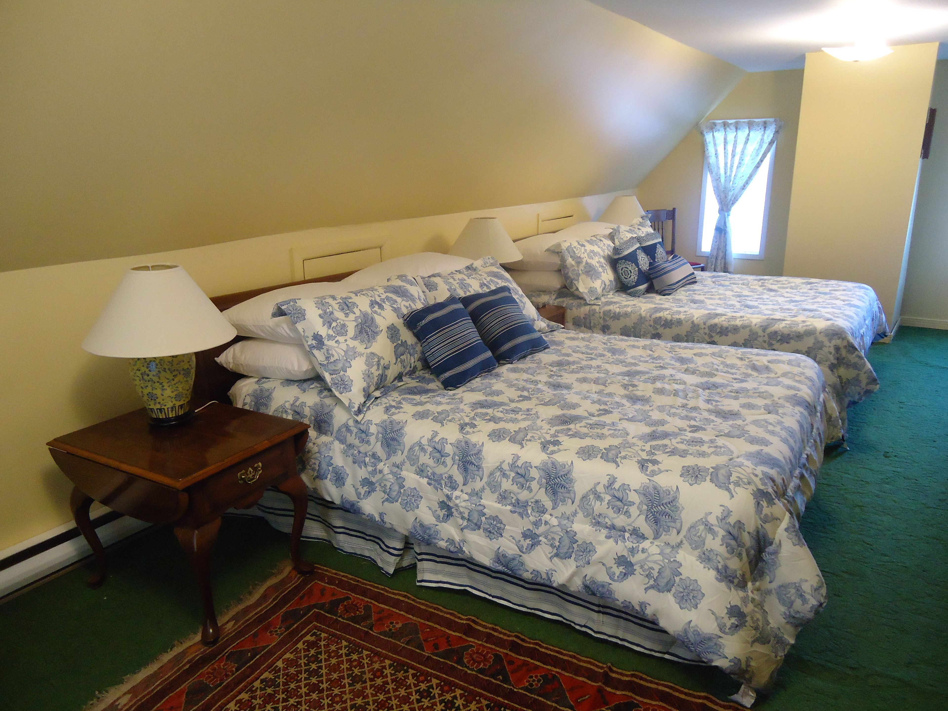 Una camera da letto con due letti, un comodino, una lampada e una finestra con tende.