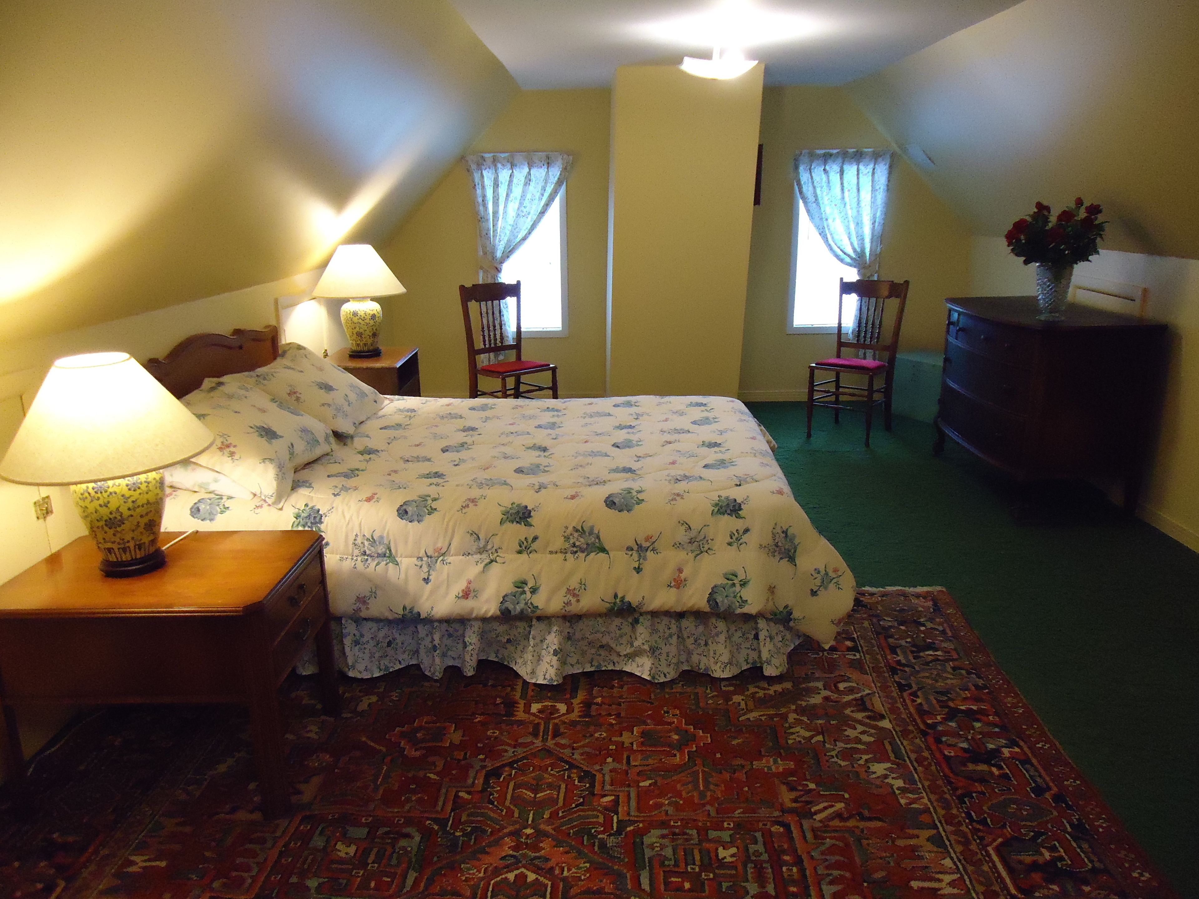 Una camera da letto con un letto, due poltrone, una cassettiera e una lampada.