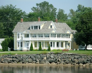 A large, two-story house with a balcony and a porch, located near a body of water.