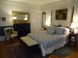 A bedroom with a large bed, a chair, a fireplace, a mirror, and a painting on the wall.