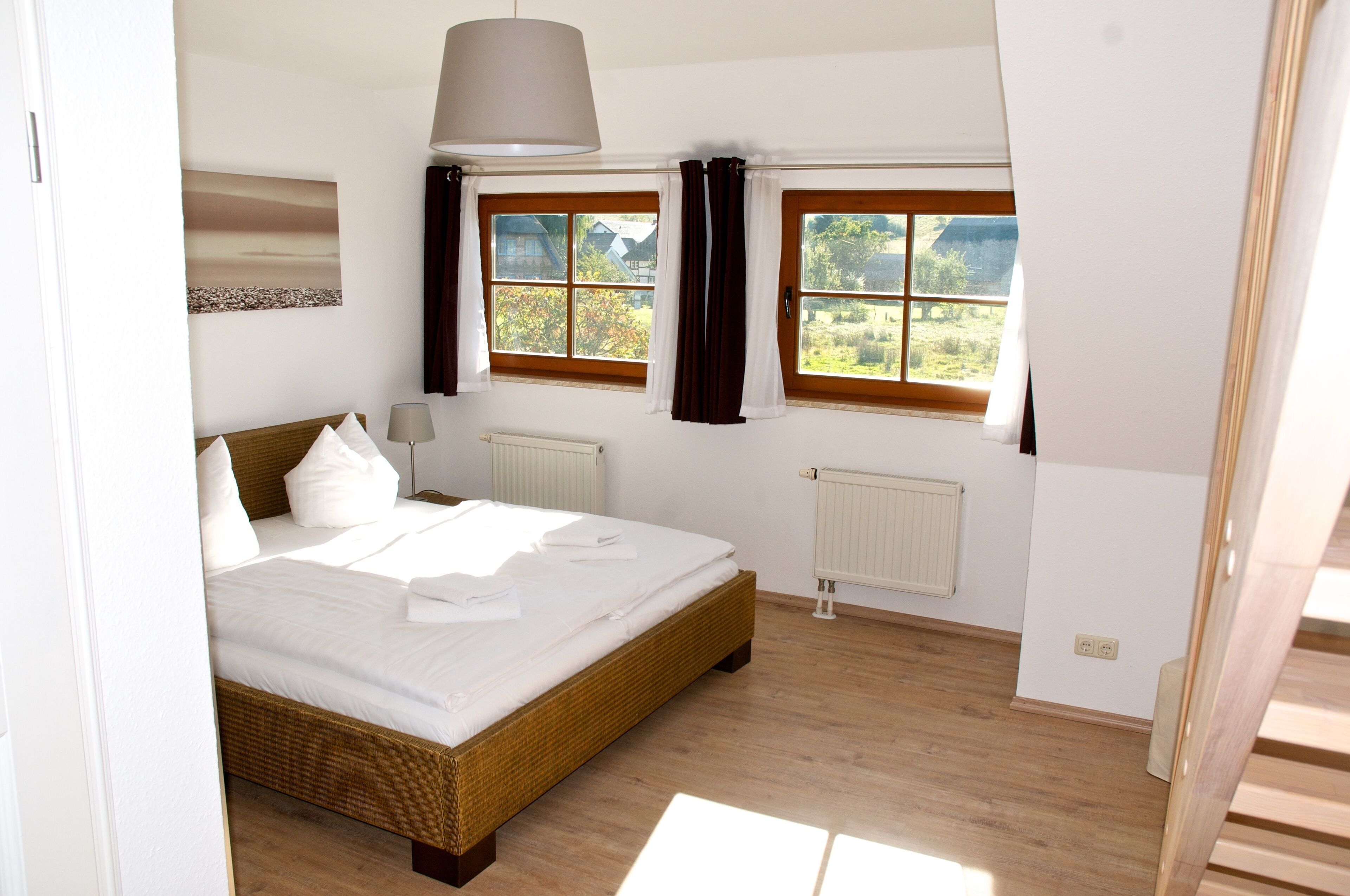 A bedroom with a bed, two windows with curtains, a radiator, and a ceiling light.