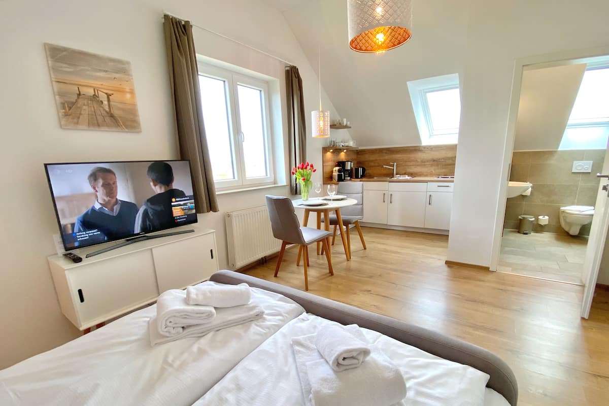 A hotel room with a bed, a TV, a dining area, and a kitchen.