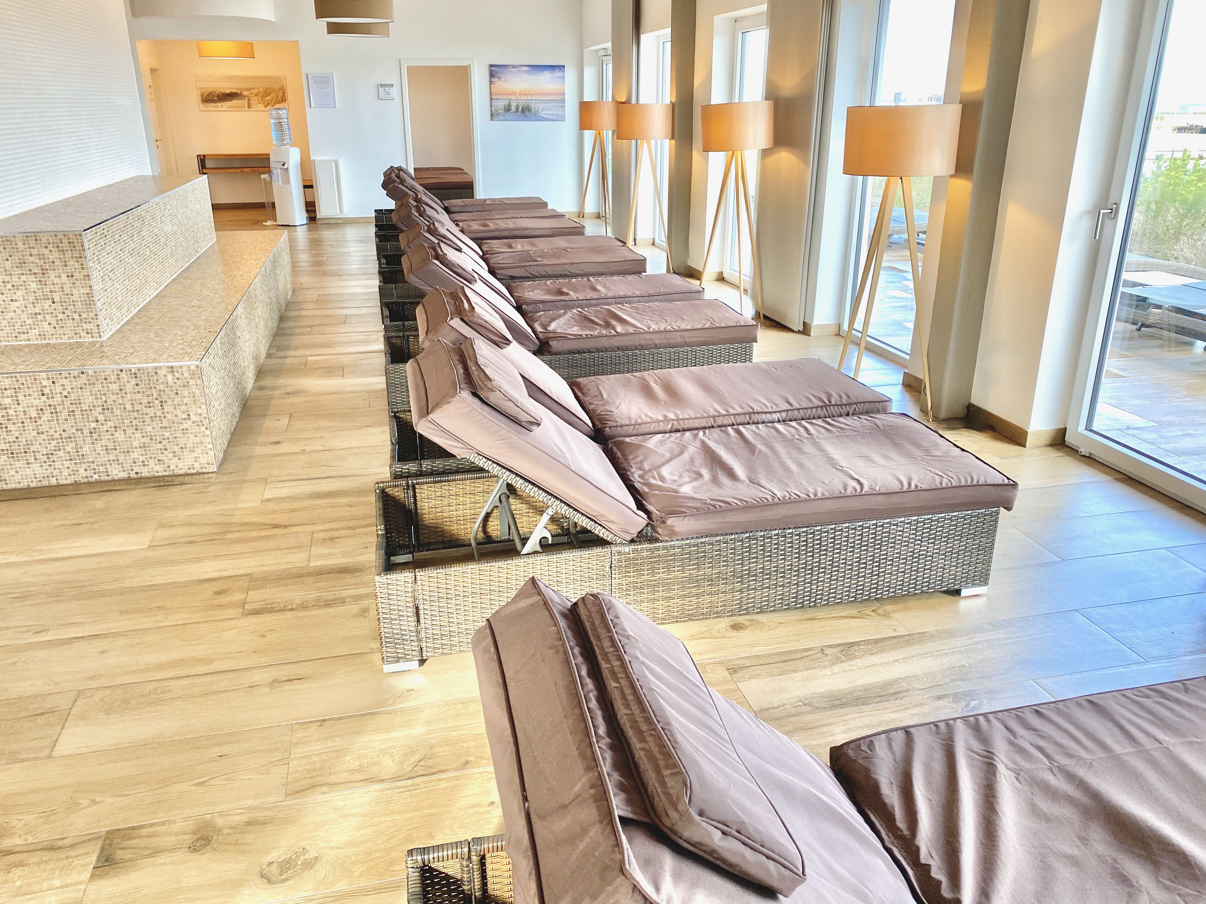 Un área de spa con varias camillas de masaje dispuestas en fila, suelo de madera y ventanas amplias que permiten la entrada de luz natural.