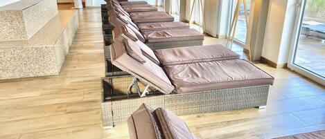 A spa area with multiple massage tables arranged in a row, wooden flooring, and large windows providing natural light.