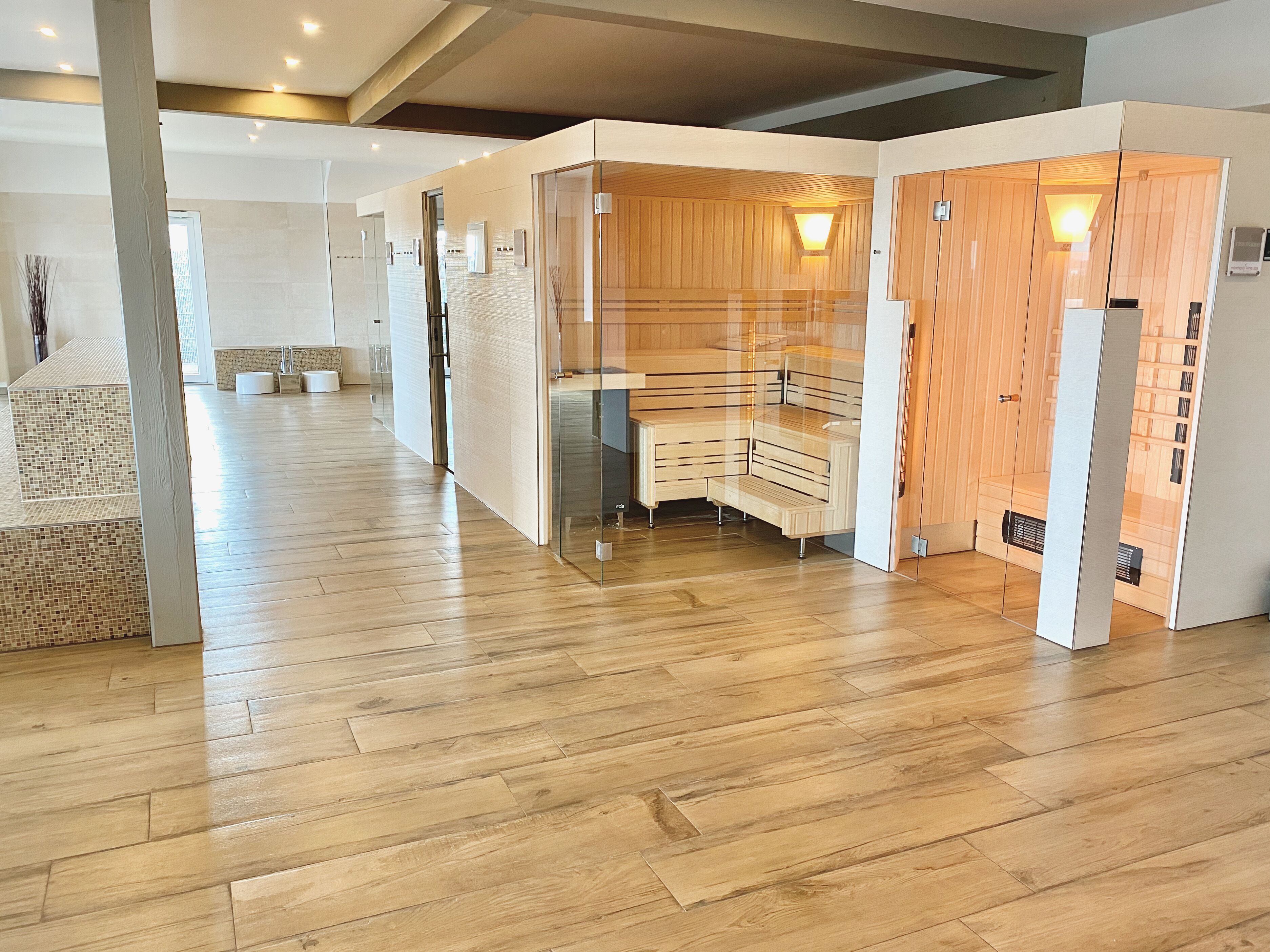 A modern hotel lobby with wooden flooring, glass partitions, and a central seating area.
