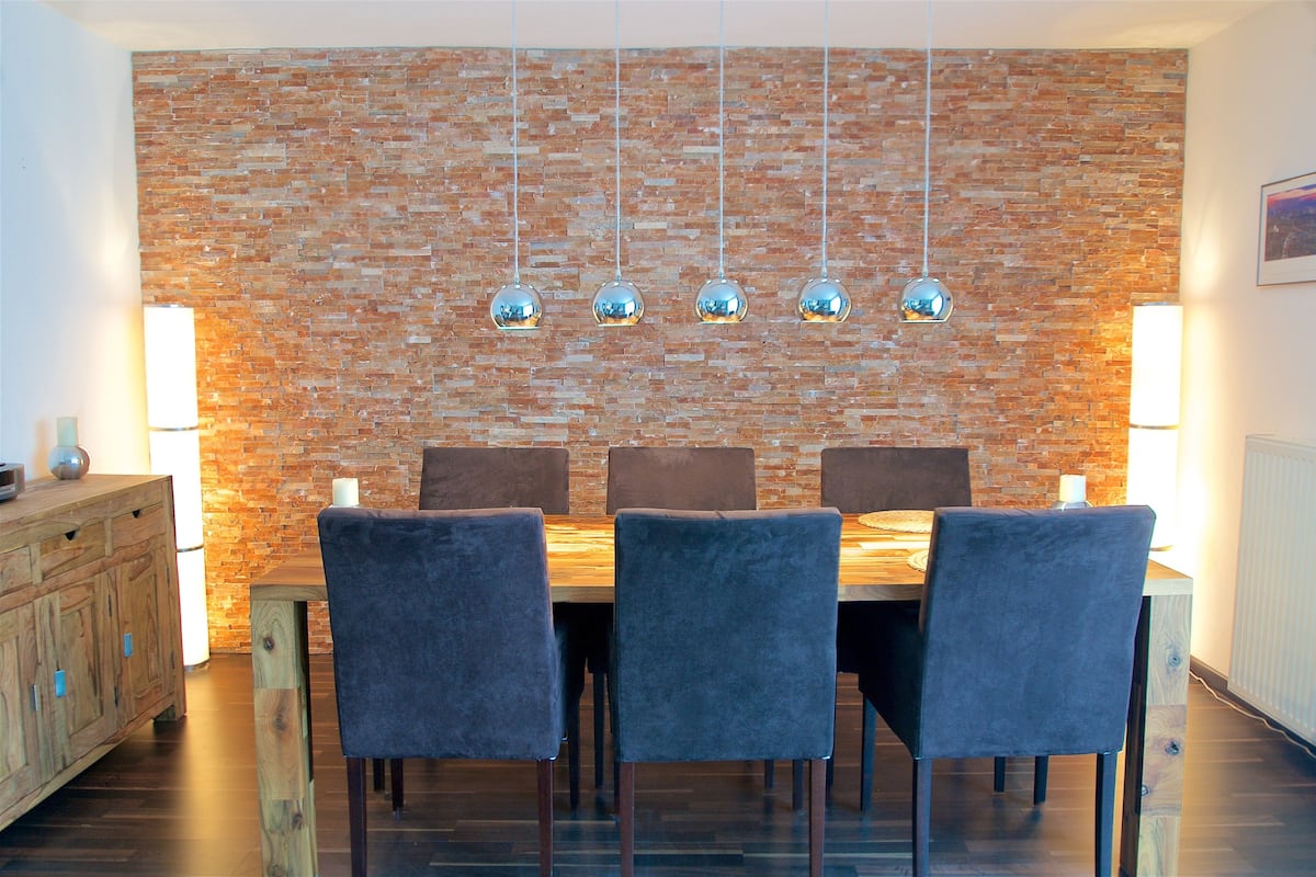 A dining area with a brick wall, hanging pendant lights, and a wooden table with chairs.
