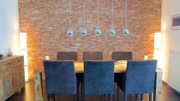 Un comedor con pared de ladrillo, lámparas colgantes y una mesa de madera con sillas.