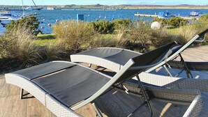A seaside patio with lounge chairs and a view of boats and a bridge in the distance. - Moenchgut Living & Spa (Mönchgut-Granitz)