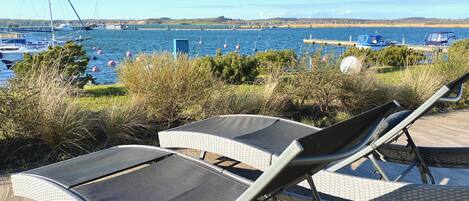 Una terrazza sul mare con poltrone relax e vista su barche e un ponte in lontananza.