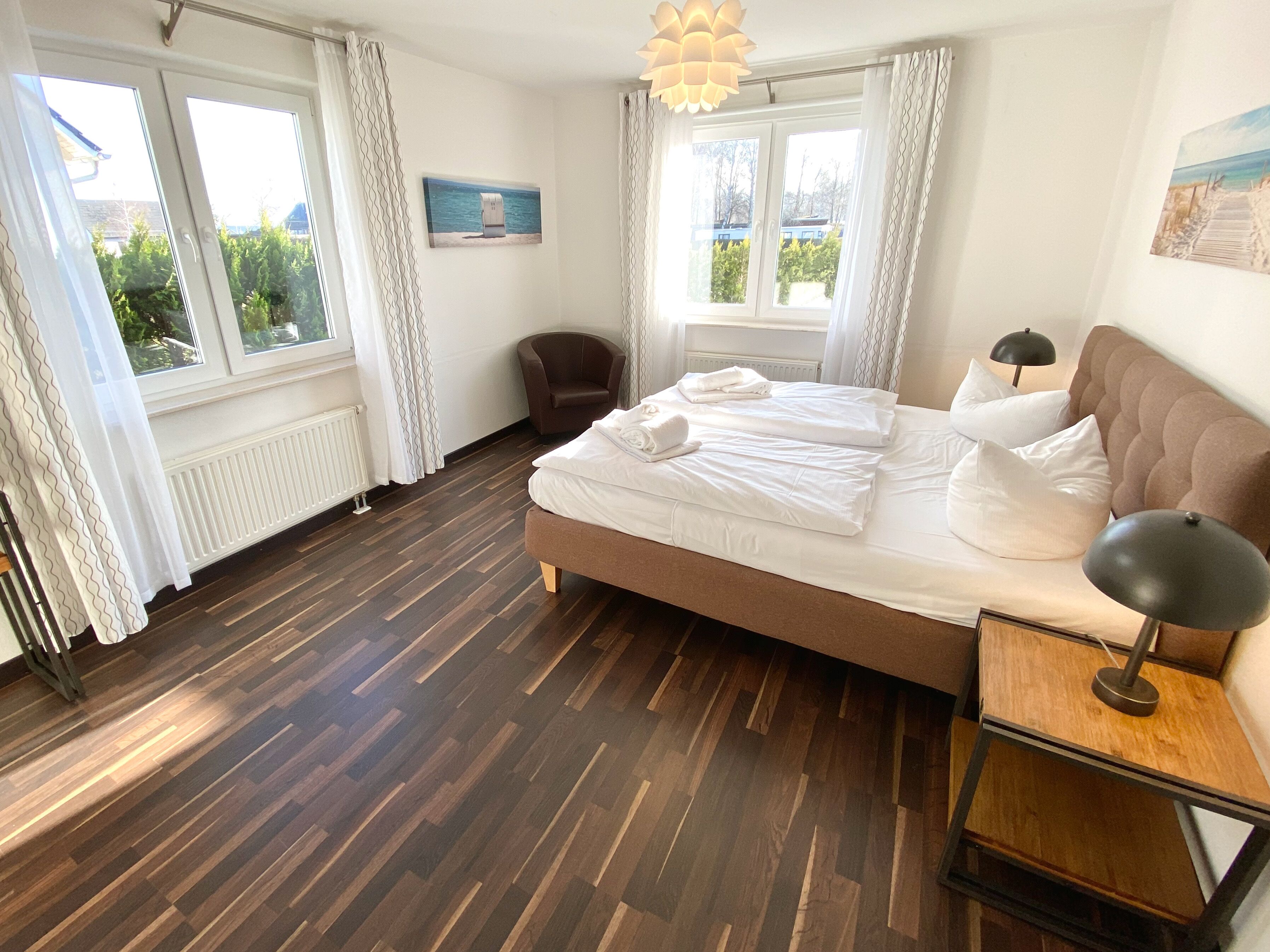 A bedroom with a large bed, a chair, a bedside table, and a view of the outdoors through the windows.