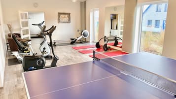 Ein Fitnessraum mit Trainingsgeräten, einem Tischtennis-Tisch und großen Fenstern.