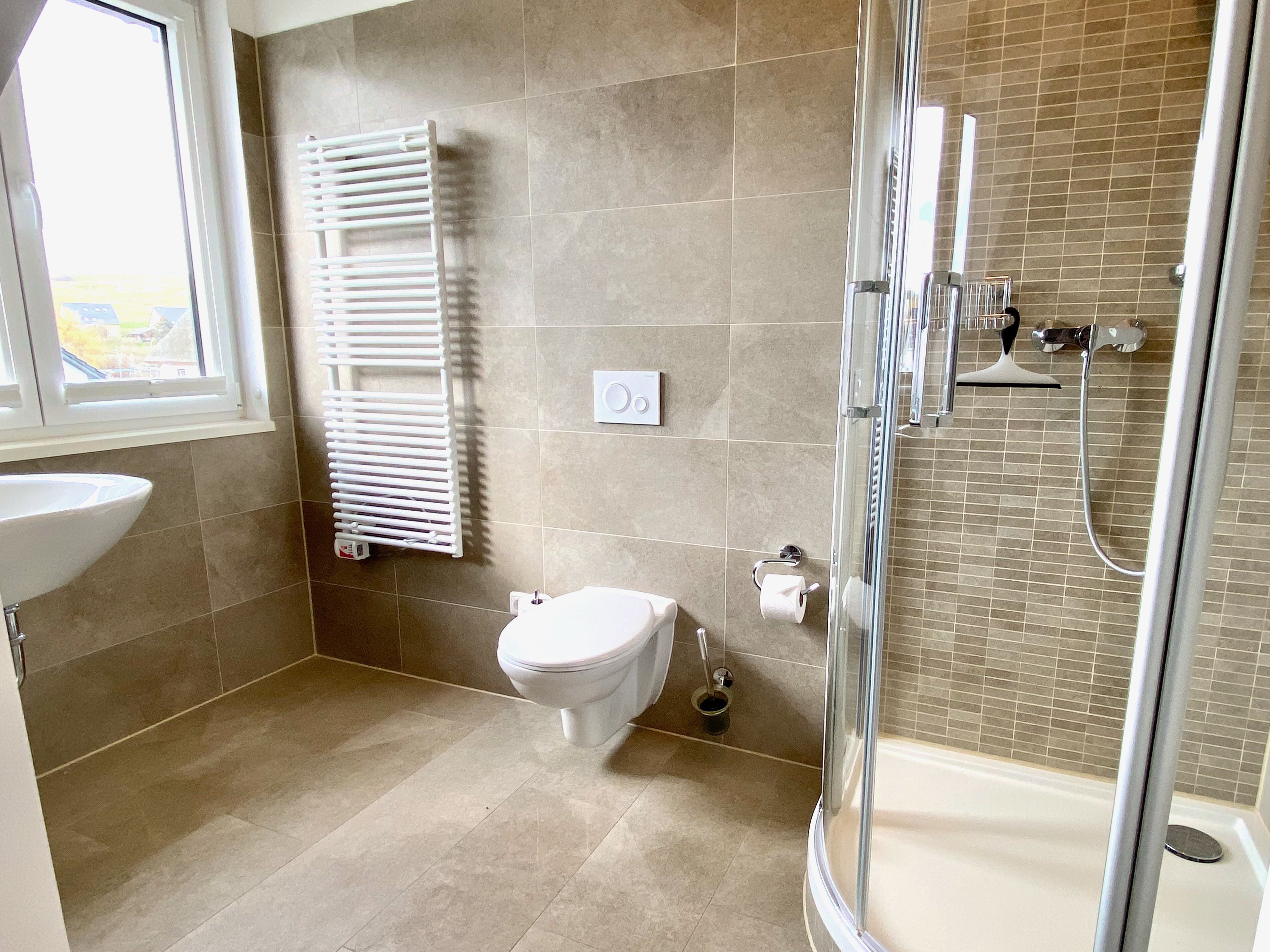 Et moderne badeværelse med toilet, bruseniche, et hvidt radiatorskab og en vask.