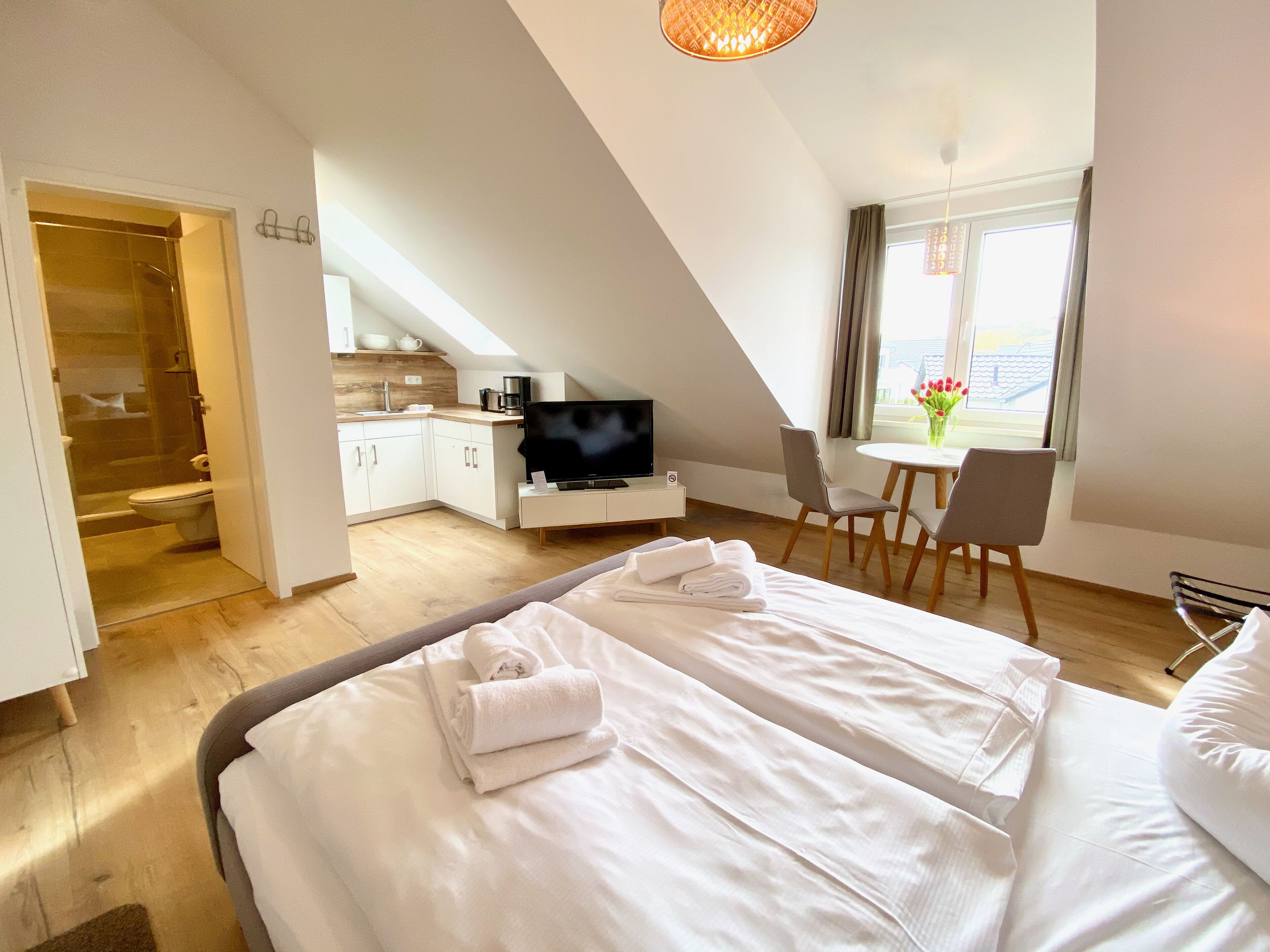 Una habitación de hotel moderna con una cama grande, televisión, pequeña cocina y zona de comedor.