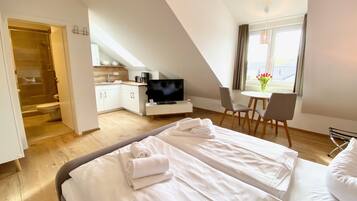 Una habitación de hotel moderna con una cama grande, televisión, pequeña cocina y zona de comedor.