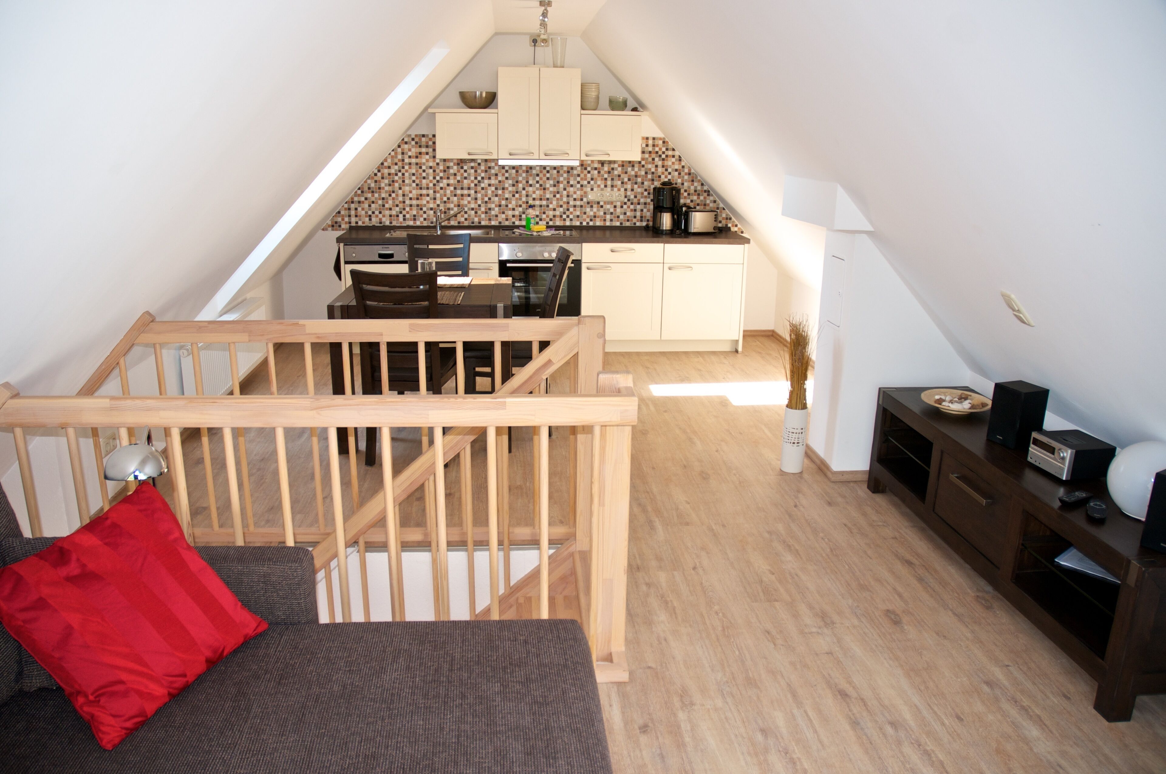 Een slaapkamer in loftstijl met een houten trap, een eethoek met tafel en stoelen, en een kitchenette op de achtergrond.