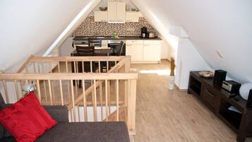 Een slaapkamer in loftstijl met een houten trap, een eethoek met tafel en stoelen, en een kitchenette op de achtergrond.