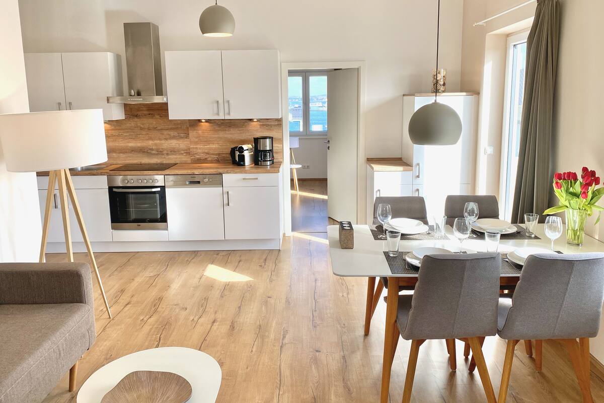 A modern kitchen with white cabinets, a wooden countertop, and a dining area with a table set for two.