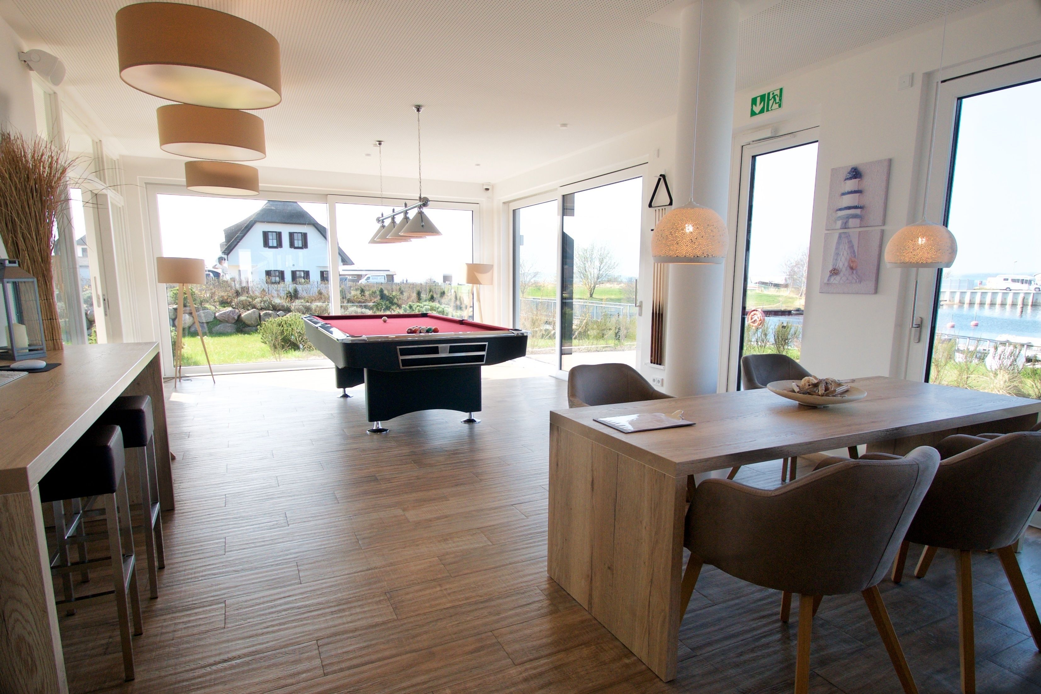A modern room with a pool table, wooden flooring, and a dining area with chairs.