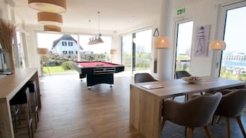 A modern room with a pool table, wooden flooring, and a dining area with chairs.