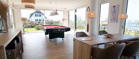 A modern room with a pool table, wooden flooring, and a dining area with chairs.