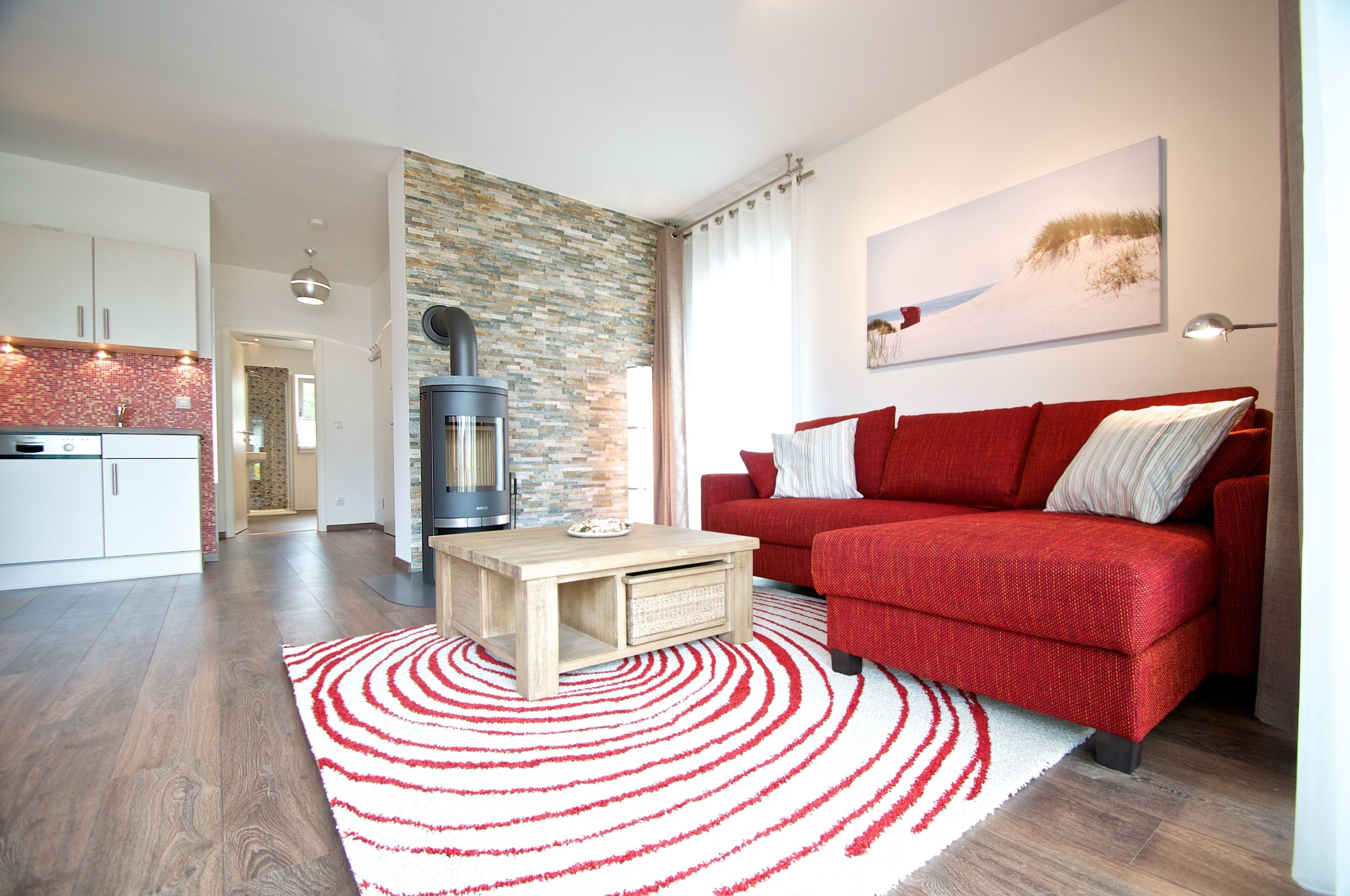 A modern living room with a red sofa, a fireplace, and a kitchen in the background.