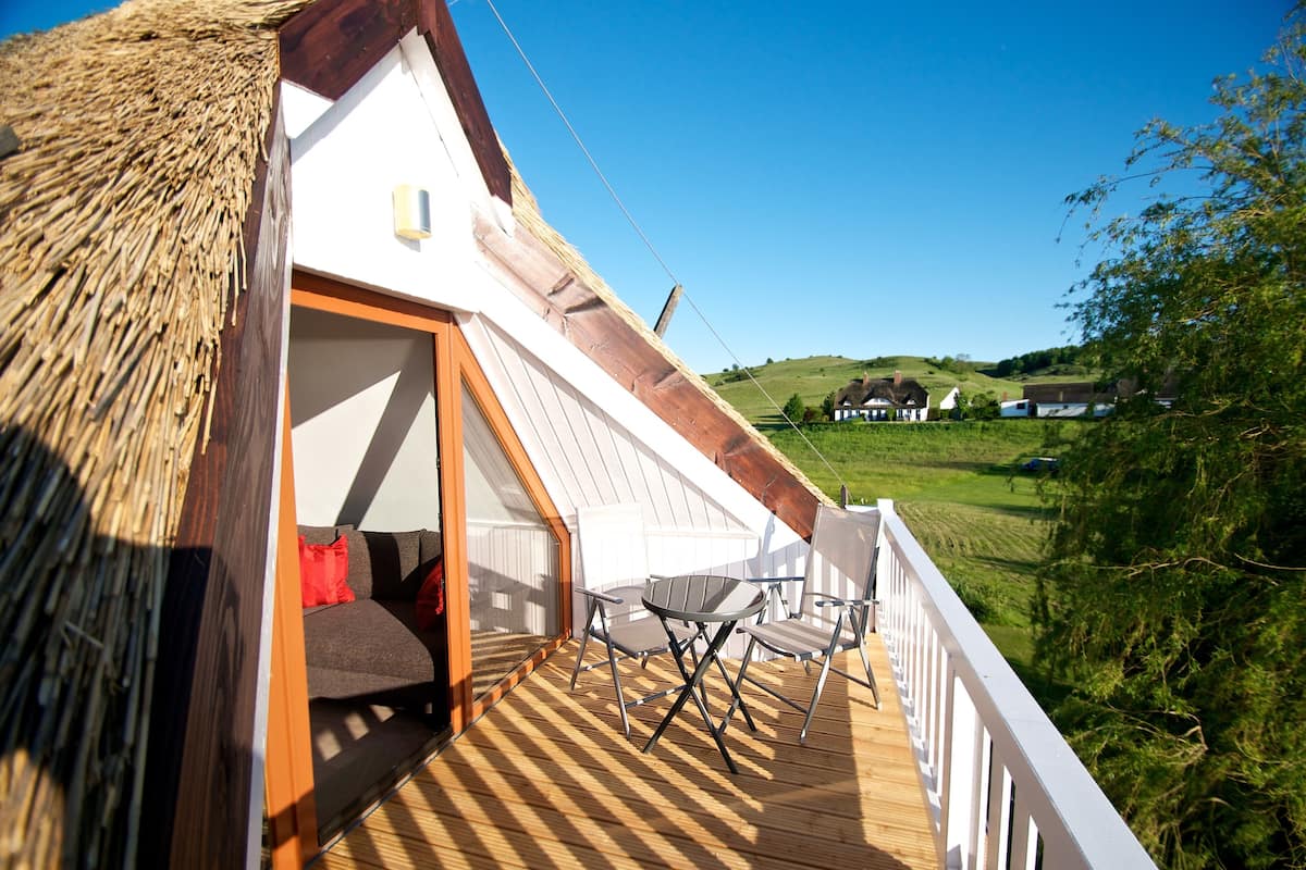 A thatched-roof room with a wooden deck, a table, and two chairs.
