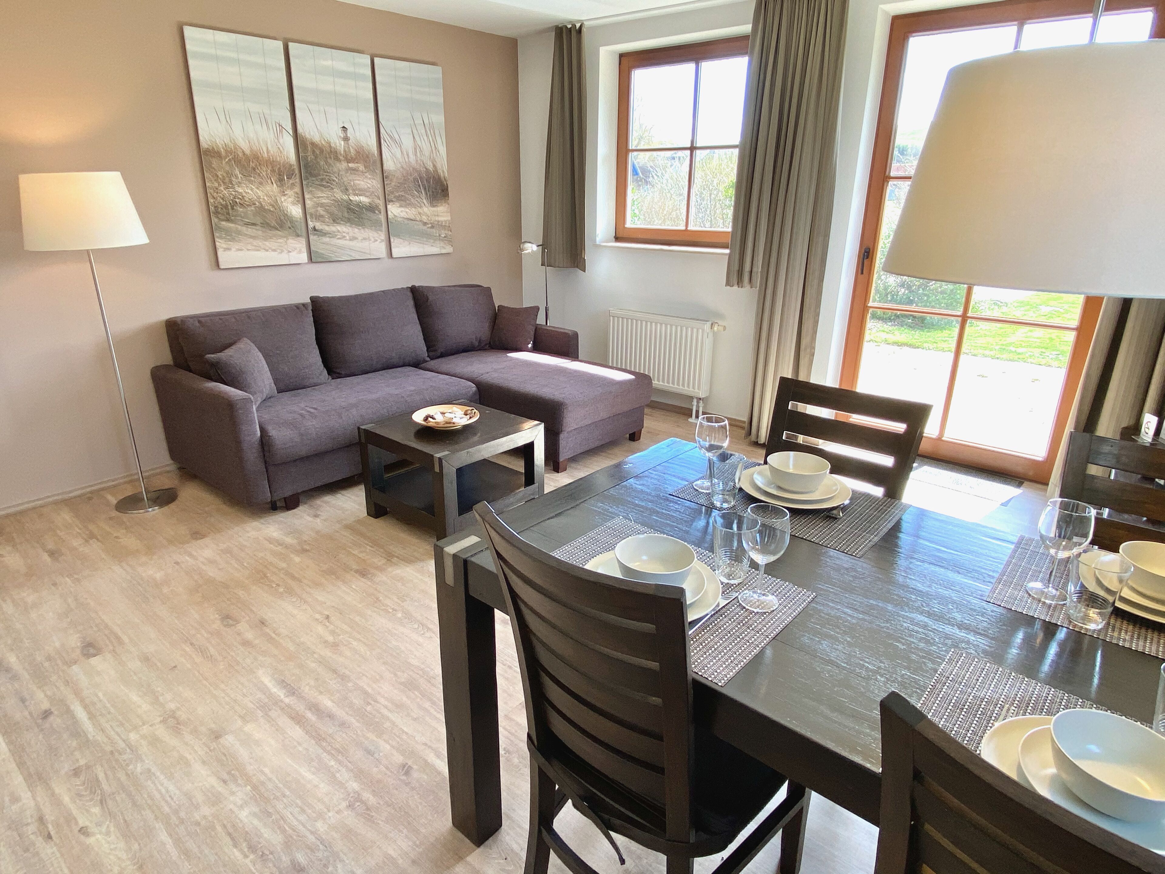 A modern living room with a sofa, a dining table set for four, and a large window with curtains.