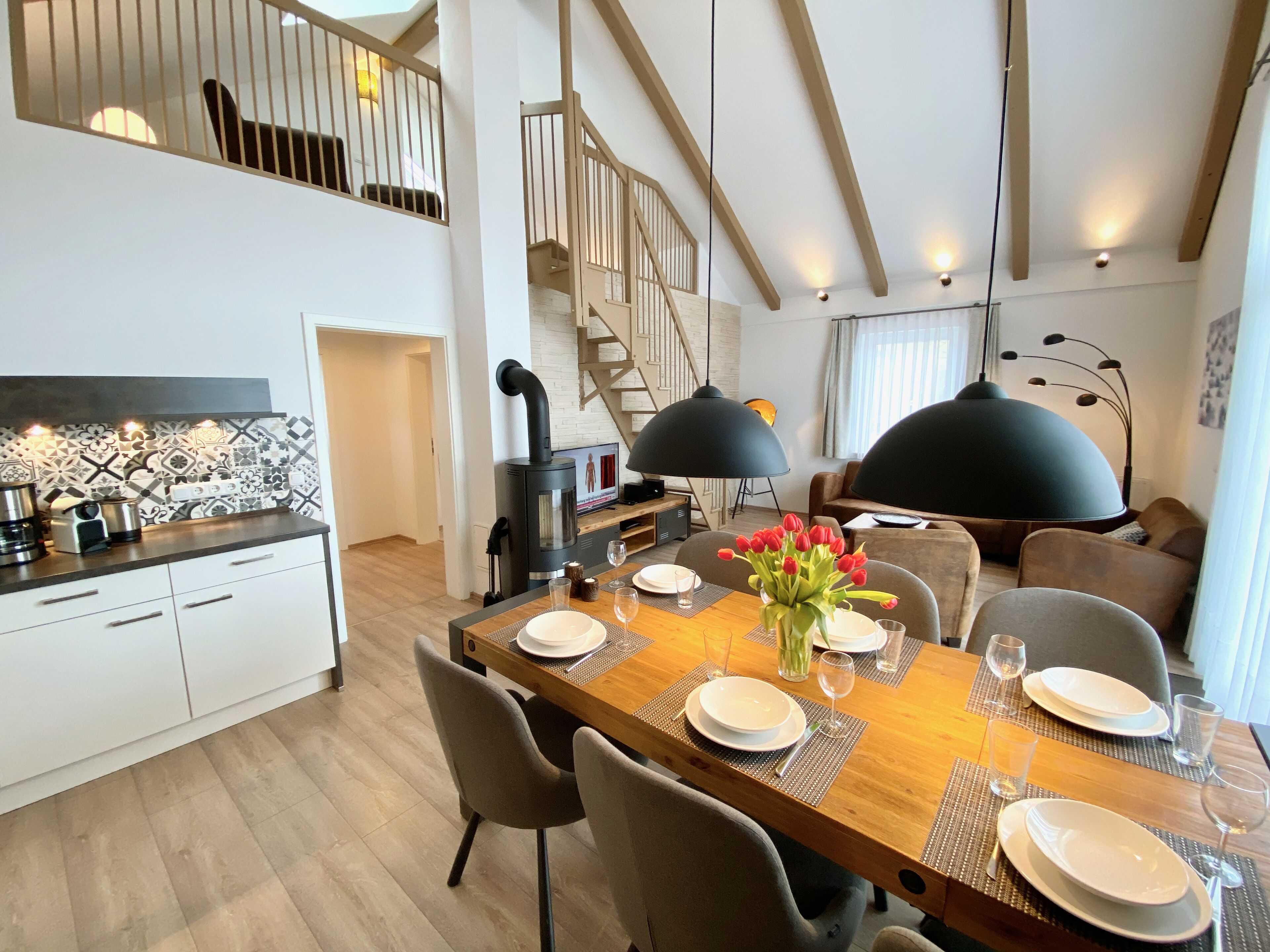 A modern kitchen with a stove, dining table set for four, and a staircase leading to an upper level.