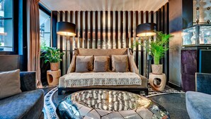 A modern bedroom with a large bed, two side tables, a round coffee table, and a view of the city. - The One Alma Paris (Paris)