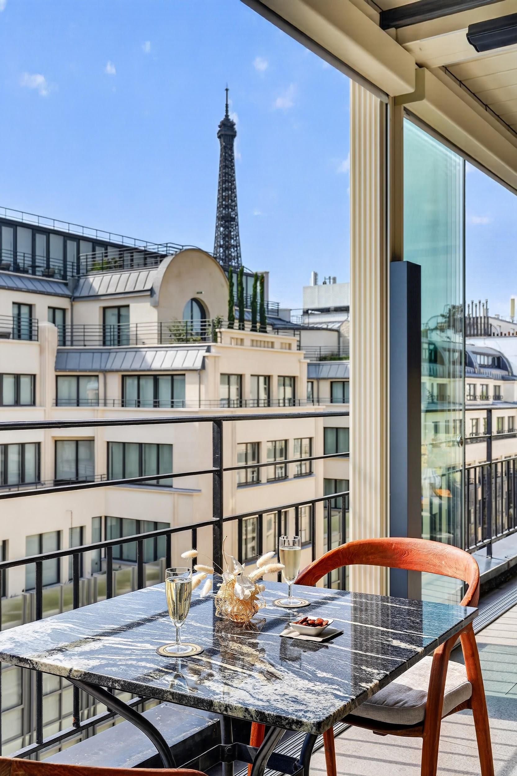 Une table avec une coupe de champagne et un centre de table décoratif, donnant sur un paysage urbain avec des bâtiments modernes et une tour.