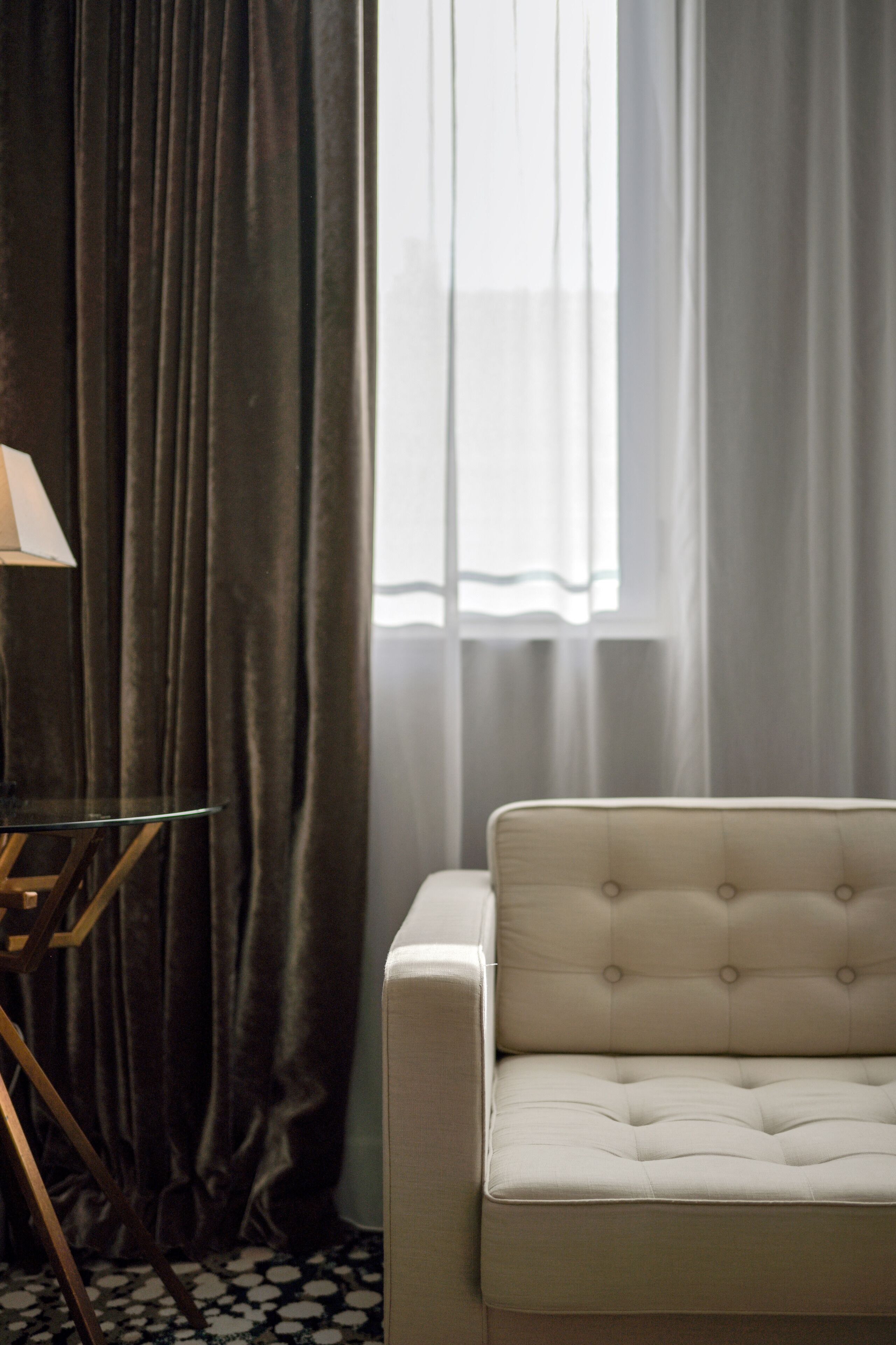 A room with a sofa, a lamp on a stand, and a window with curtains.