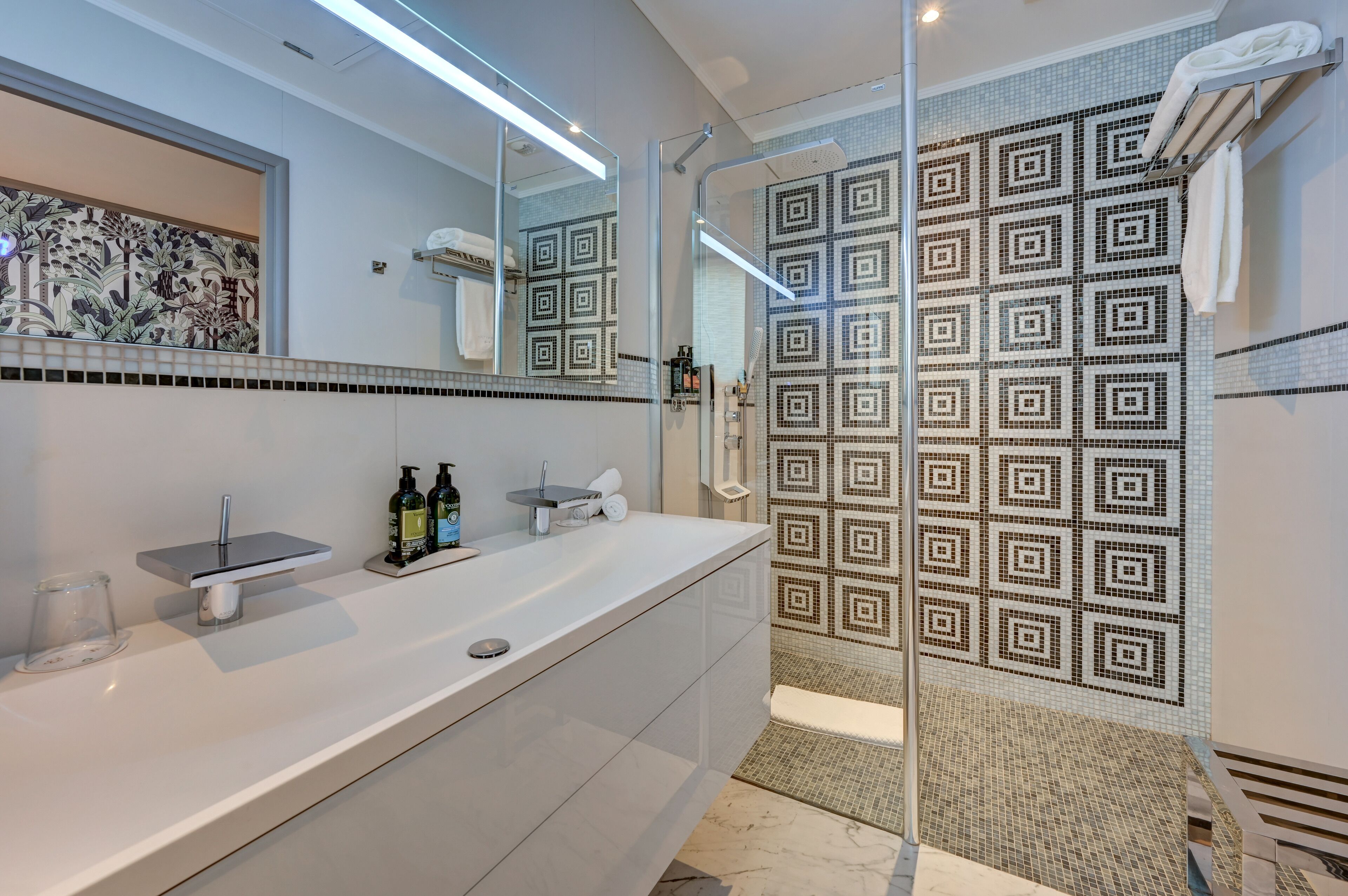 Une salle de bain moderne avec un grand miroir, une douche en verre et un mur recouvert de carreaux décoratifs.