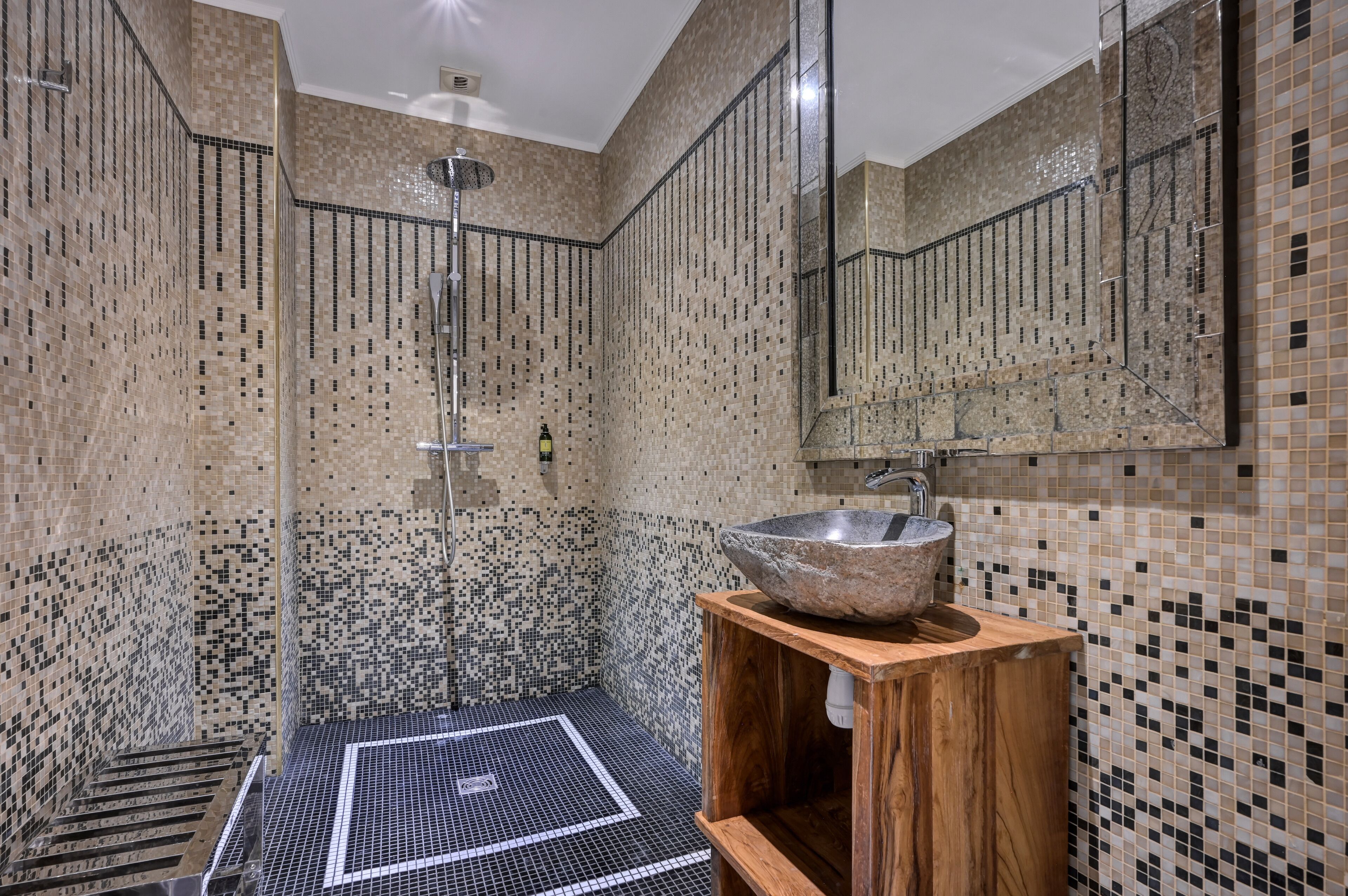 Un baño moderno con paredes de mosaicos, un lavamanos grande y una ducha a pie.