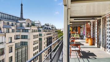 Varanda com vista para prédios parisienses, incluindo a Torre Eiffel, e interior moderno com móveis e objetos decorativos.
