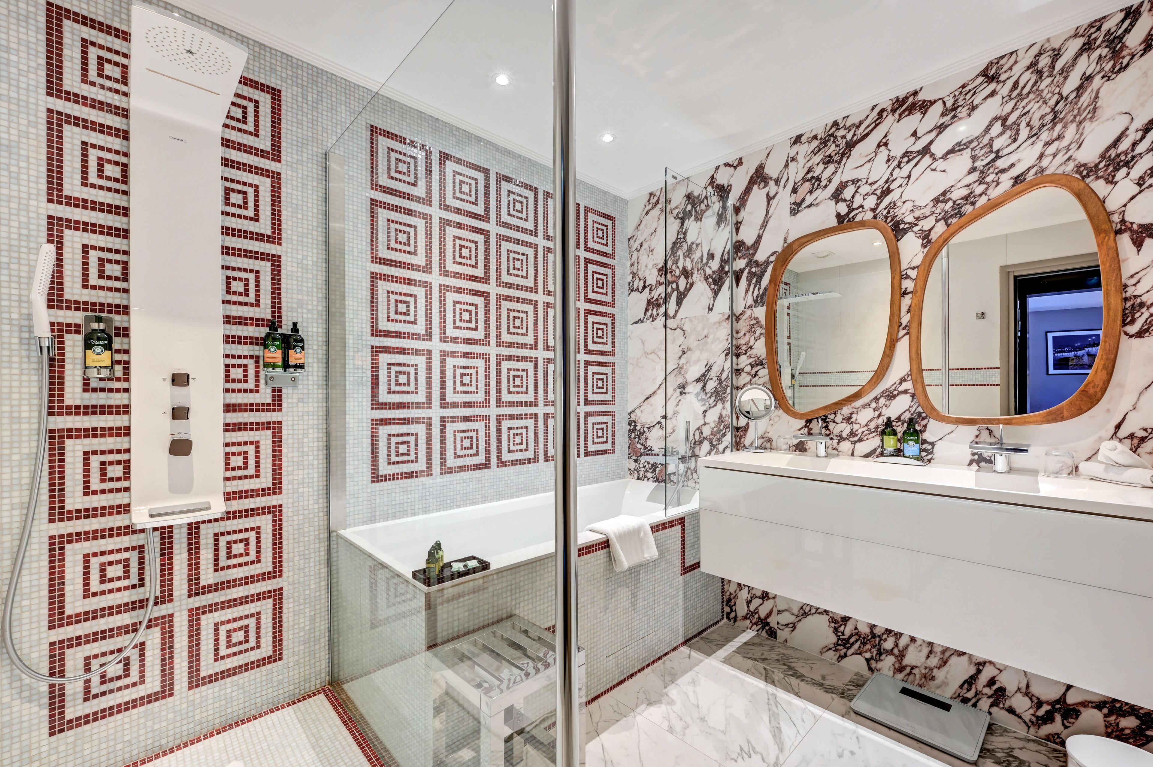 A modern bathroom with patterned tiles, a glass shower enclosure, a marble vanity, and a large mirror.