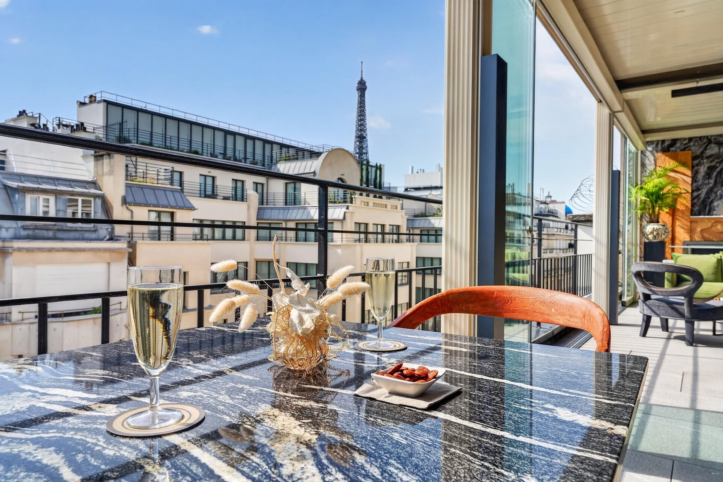 Un balcon avec une table en verre, deux coupes de champagne, des plumes décoratives et un bol de collations.