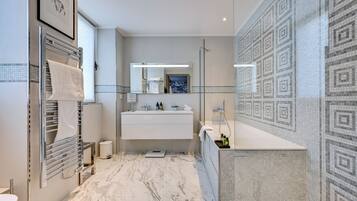 A modern bathroom with a marble floor, a large mirror, a white sink, and a shower area.