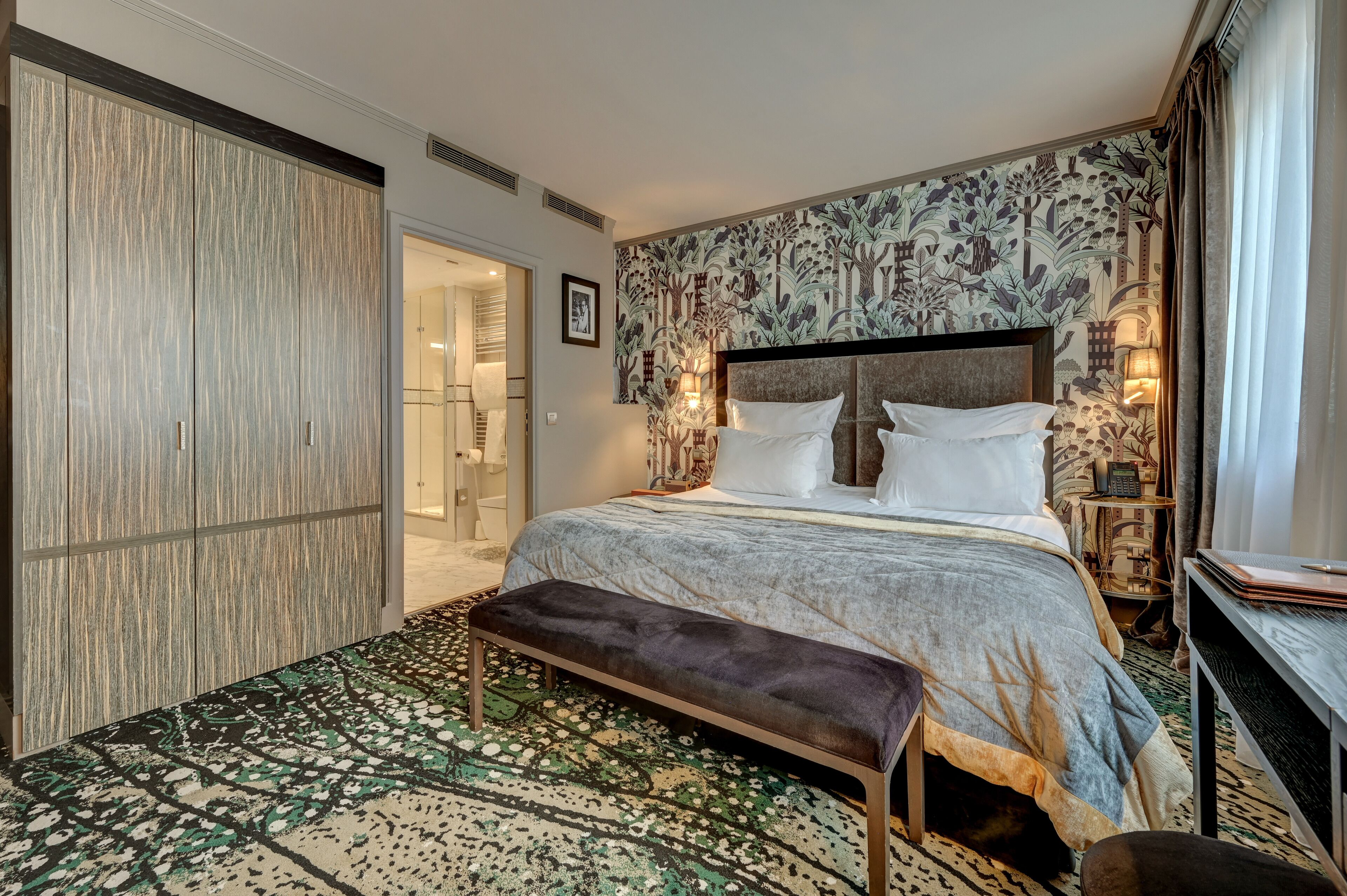 Camera d'albergo con un letto grande, una panca, una scrivania e un tappeto decorato.