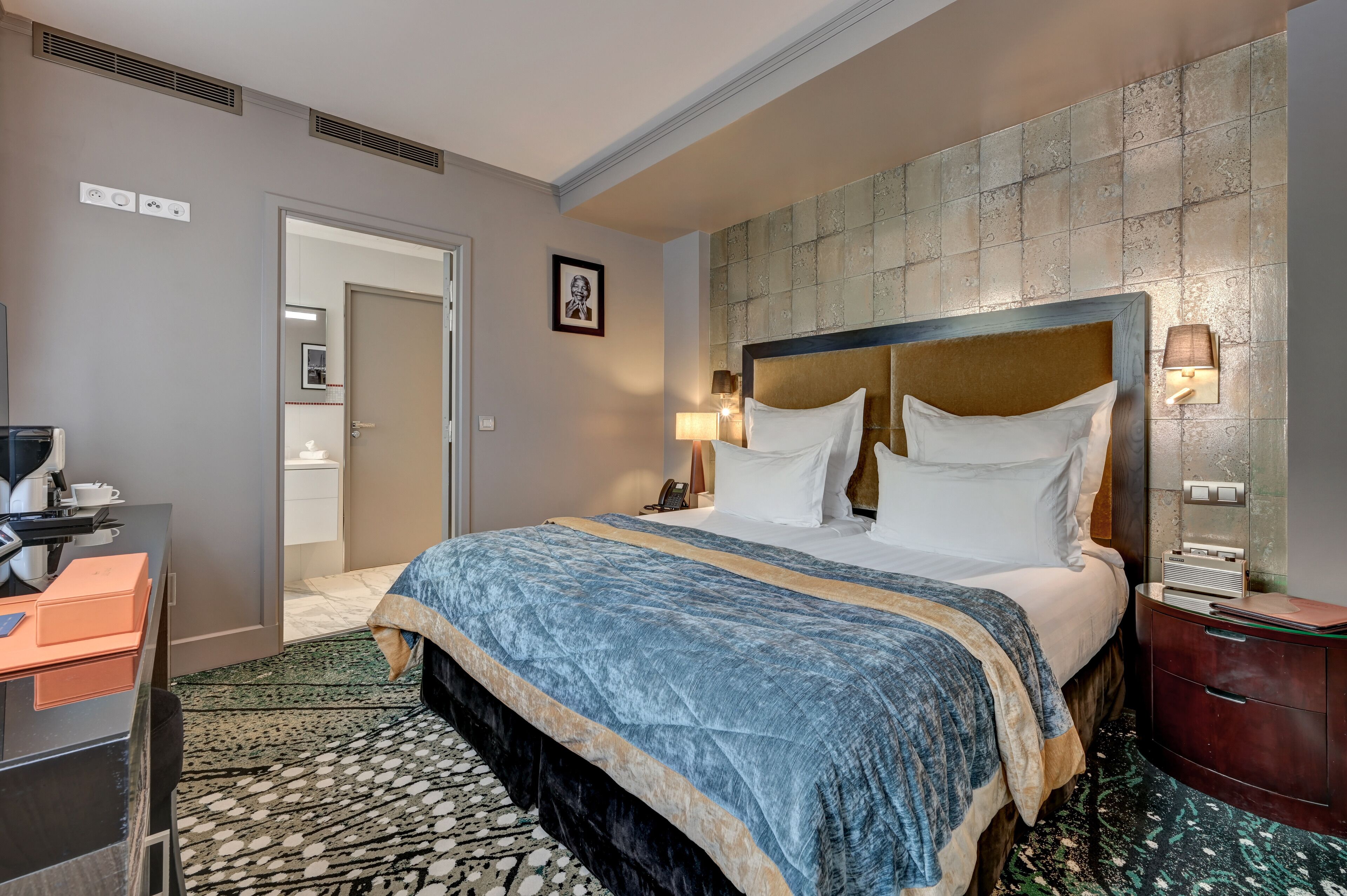 Habitación de hotel con una cama grande, un escritorio con computadora, teléfono y mesita de noche con lámpara.