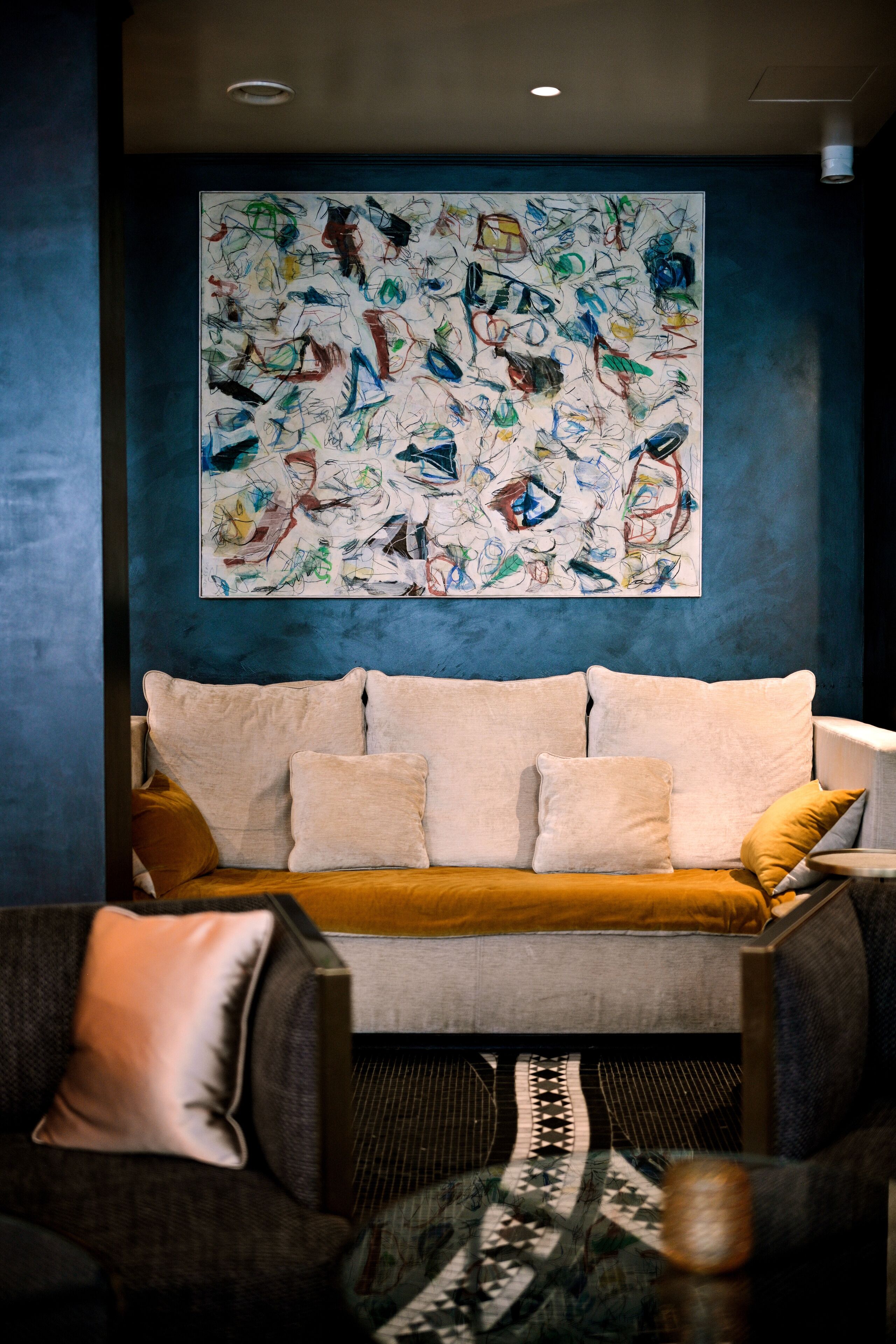 A modern living room with a sofa, two armchairs, and a patterned rug. A large abstract painting adorns the wall above the sofa.