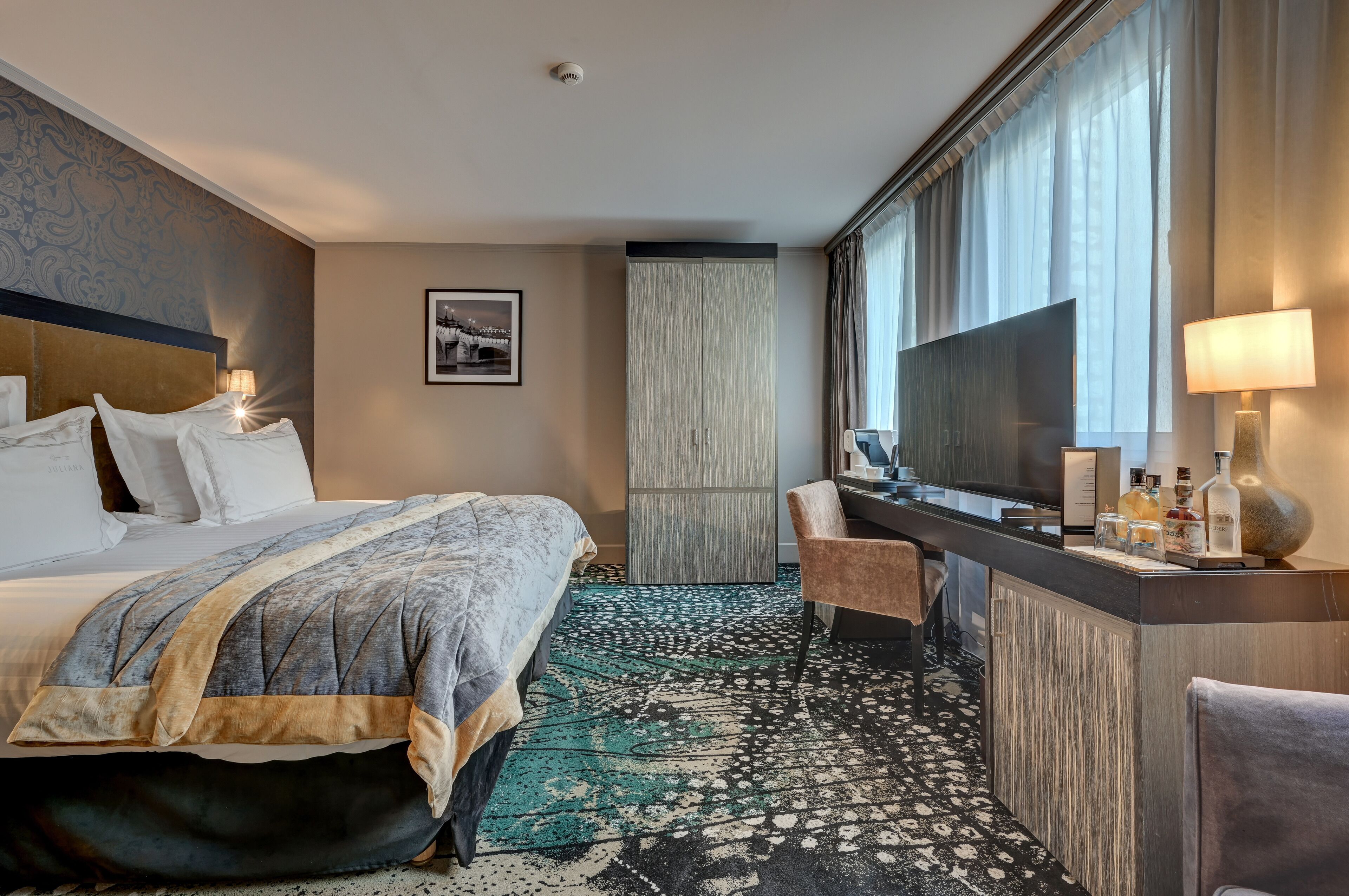 Ein Hotelzimmer mit einem großen Bett, einem Schreibtisch mit Stuhl, einem Fernseher und einer Minibar.