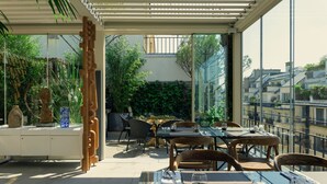 An outdoor dining area with tables and chairs, a glass wall, and a view of buildings.