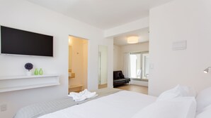 Una habitación de hotel moderna con una cama grande, un televisor de pantalla plana montado en la pared y un pequeño rincón de descanso con un sofá y una mesa.