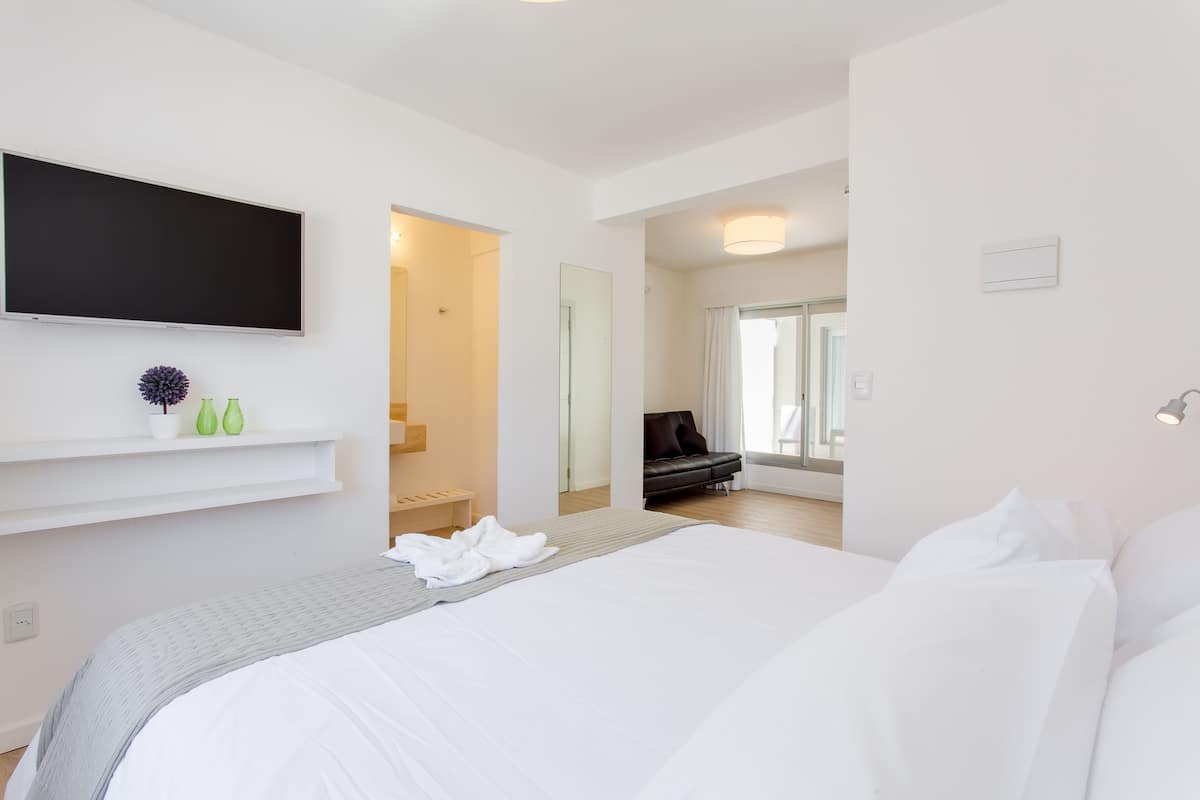 Una habitación de hotel moderna con una cama grande, un televisor de pantalla plana montado en la pared y un pequeño rincón de descanso con un sofá y una mesa.