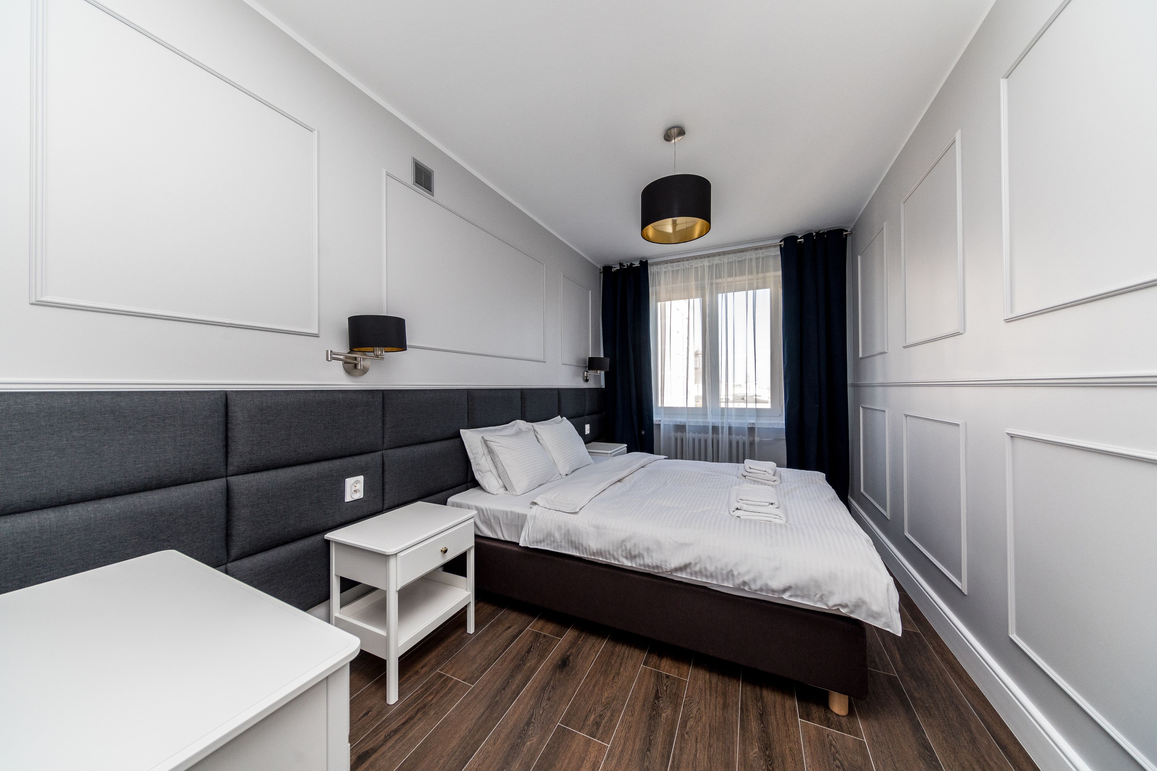 Ein modernes Schlafzimmer mit einem großen Bett, Nachttischen, einer Nachttischlampe und einer Pendelleuchte.