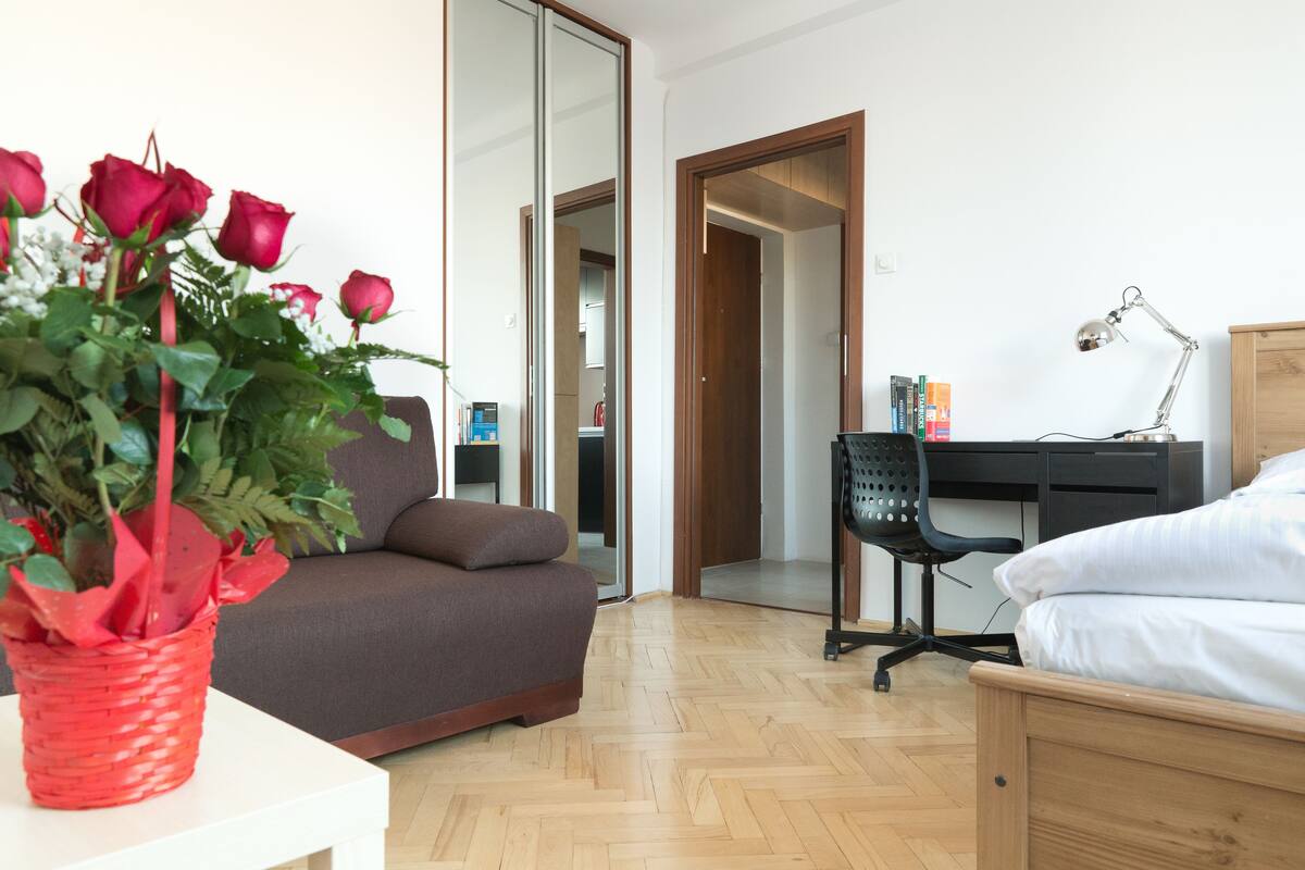 Un dormitorio moderno con una cama de madera, un escritorio con una silla, un sofá y un espejo grande.